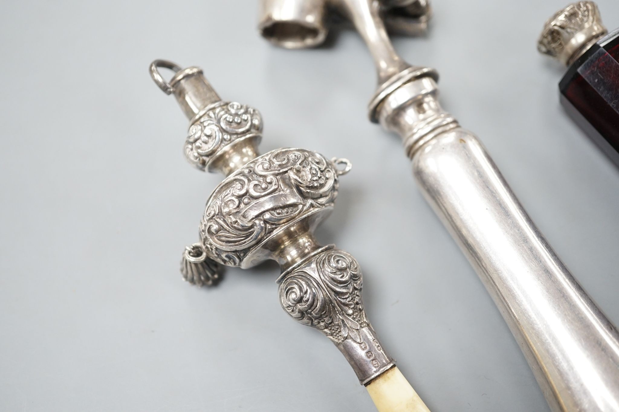 A silver mounted rattle, a white metal mounted double ended ruby glass cent bottle and a silver plated handled roast joint holder.
